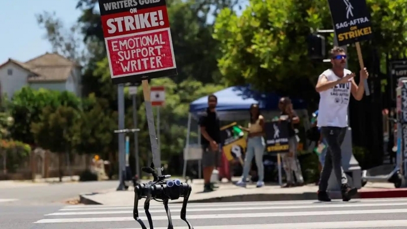 Un robot care ține o pancardă în timpul protestelor actorilor și scenariștilor din fața studiourilor Paramount